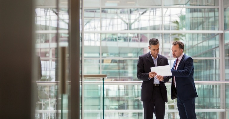 Two men in suits discussing a printout, suggesting data in light of new tax law